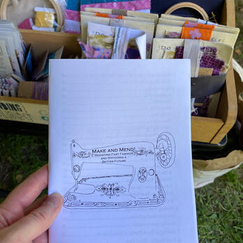 Make and Mend Zine held in a hand with some mending kits behind