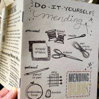 &quot;Do It Yourself Mending&quot; zine held with cover page showing and part of back page