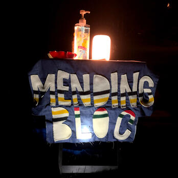 small table with mending bloc sign, handmade with letters cut from reclaimed blanket remnants, with light on top, in the dark