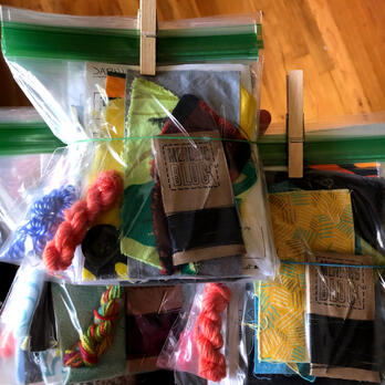 mending kits in ziplock bags, with small amounts of thread, yarn, and fabric inside