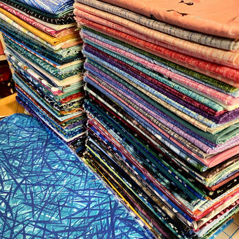 two big stacks of colorful patterned fabric, and more fabric in front of the stacks