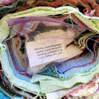 many pieces of fabric rolled up together, and a ziplock bag of water beads in the center