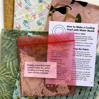 the components of a cooling scarf kit: six pieces of fabric, a ziplock bag with dry beads inside, and a printed instruction book