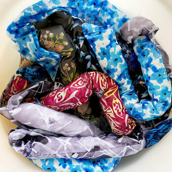 several (at least seven) cooling scarves in a bucket of water, looking straight down at them, in different fabrics